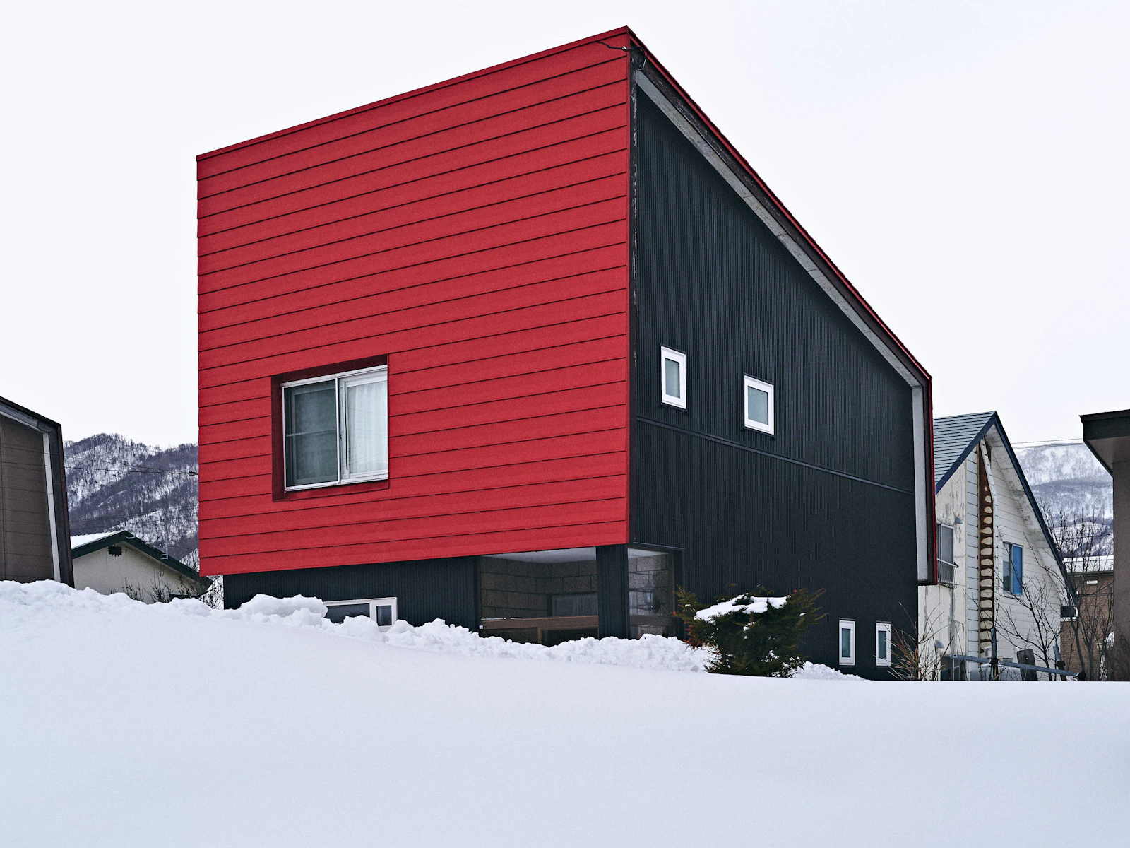 Illustrative photo of a modern house with red and black siding in a snowy landscape