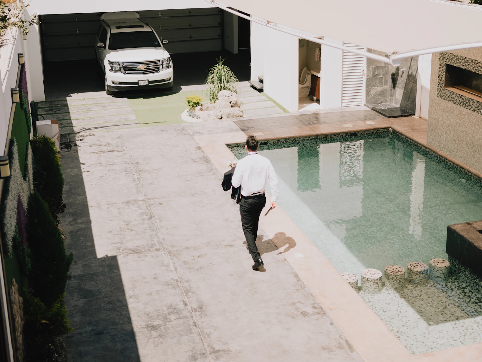 Illustrative photo of a man walking toward a swimming pool and modern home