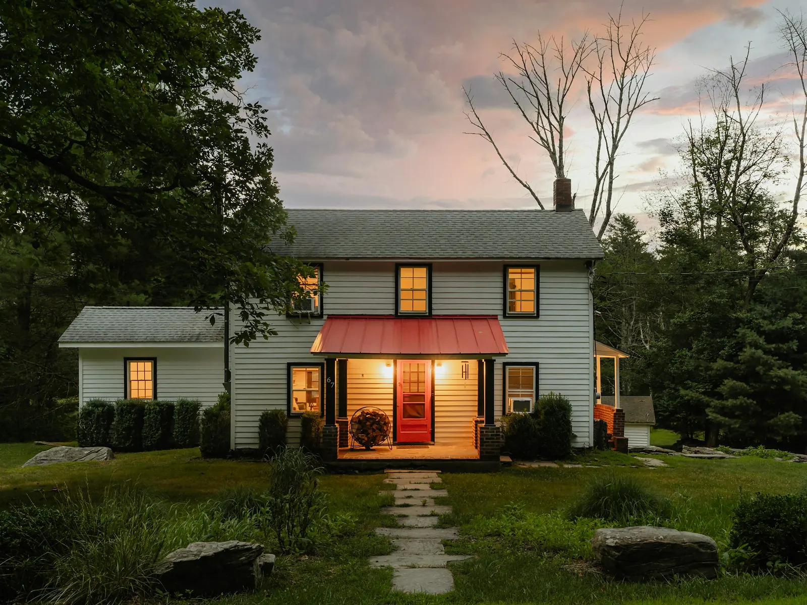 Illustrative photo of a classic clapboard house with a red door awning at dusk